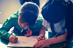 Two girls bent close over one sheet, drawing with pencils. Bogotá, Colombia, 2011.