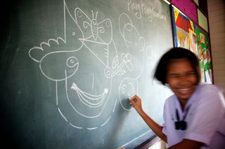 A laughing girl draws on a blackboard covered in chalk shapes. Thailand, 2011.