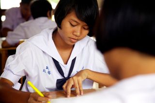 A student in a white school uniform draws with a yellow pen. Thailand, 2011.