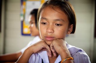 A girl in a school uniform rests her chin on her hands, thinking. Thailand, 2011.