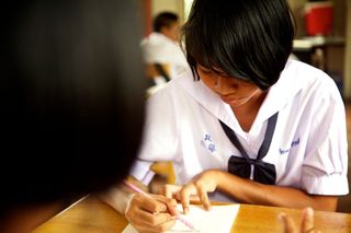 A student in a white uniform draws with a pink pencil. Thailand, 2011.