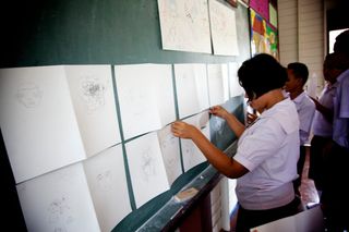A student pins drawings of faces to a green board. Thailand, 2011.