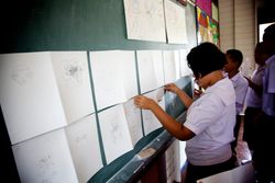 A student pins drawings of faces to a green board. Thailand, 2011.