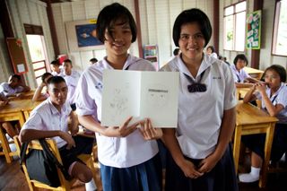 Two students hold up a sheet with two drawn faces side by side. Thailand, 2011.