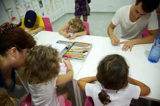 Children and adults drawing at white tables with a tray of pencils. Barcelona, Spain, 2010.