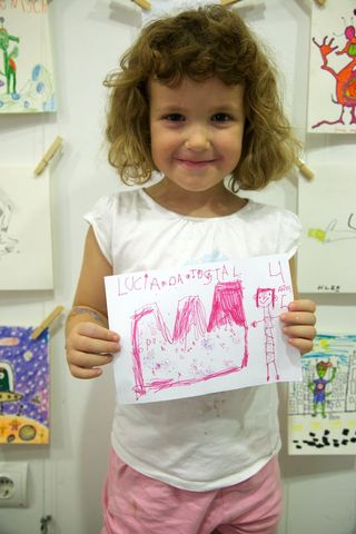 A girl holds up her pink drawing in front of a wall of pinned drawings. Barcelona, Spain, 2010.