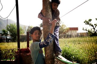 A boy looks back from a tree trunk while another boy climbs it. Rishikesh, India, 2010.