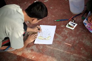 A boy kneels on a red floor, drawing with a black pen. Rishikesh, India, 2010.