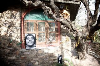 Black and white portraits hung on an old tree and a stone house. Rishikesh, India, 2010.