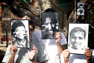 Three people hold framed black and white portraits in front of their faces. Rishikesh, India, 2010.