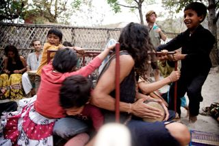 Adults and children play together in a crowd outdoors, a boy leaping. Rishikesh, India, 2010.