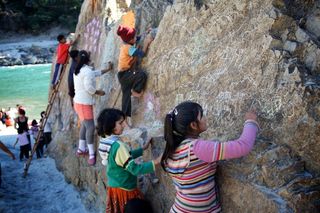 Children draw with chalk on a long rock face beside a river. The Ideal Place, 2011.