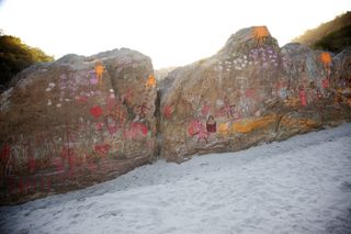 Two large boulders on white sand, covered in pink, red and yellow paintings. The Ideal Place, 2011.
