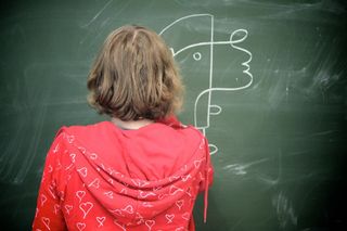 A girl in a red hoodie stands at a blackboard with a chalk face drawn on it. Brandenburg, Germany, 2010.