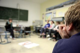 A boy watches with his hand at his mouth, the circle of students blurred behind. Brandenburg, Germany, 2010.
