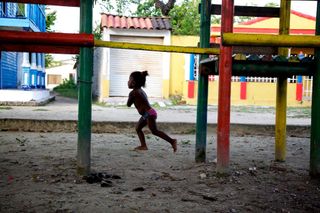 A child runs across a sandy playground between coloured climbing bars. Barú, Colombia, 2011.