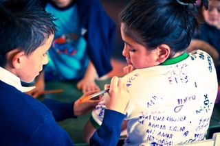 A boy and a girl drawing side by side; her white shirt is covered in handwriting. Bogotá, Colombia, 2011.