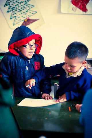 Two boys in blue jackets, one in a red hood, looking at a sheet of paper on the table. Bogotá, Colombia, 2011.