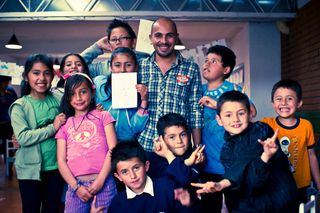 A group of children and a man pose together, one girl holding up a sheet of paper. Bogotá, Colombia, 2011.
