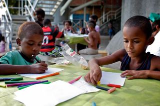 Two boys drawing with felt-tip pens at a green table. Brazil, 2012.