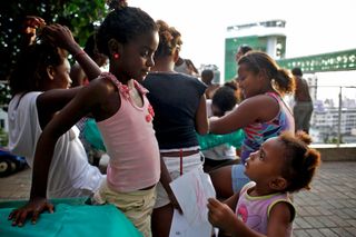 Girls gathered at a table on a terrace, one reaching over to draw. Brazil, 2012.