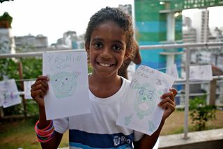 A girl holds up two drawings of aliens on the terrace. Brazil, 2012.