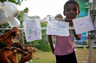 Drawings pegged on a line on the terrace, a boy standing behind them. Brazil, 2012.