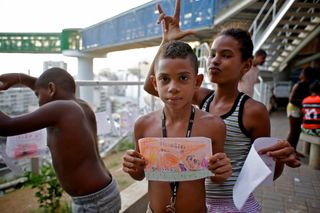 A boy holds up a long orange drawing on the terrace, friends behind him. Brazil, 2012.