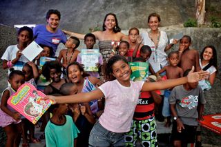 A big group of children and adults, a girl in front holding up a picture book. Brazil, 2012.