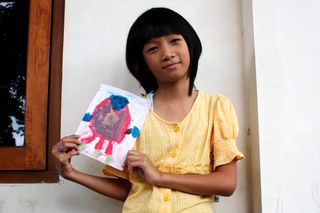 A girl in a yellow dress holds up a painted round alien. Indonesia, 2011.
