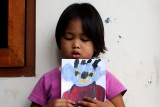 A girl holds a painting of a blue alien with horns. Indonesia, 2011.