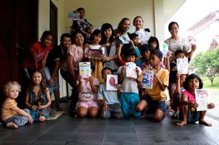 A large group of children and adults on a porch, many holding drawings. Indonesia, 2011.
