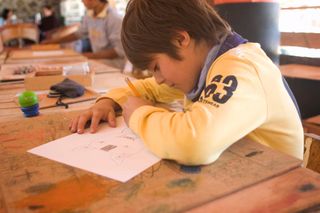 A boy in a yellow sweater draws at a paint-stained wooden table. Mexico, 2011.