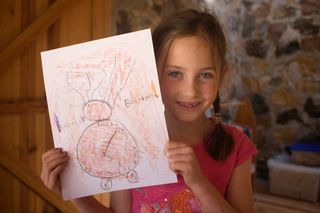 A girl holds up her pencil drawing of a round alien against a stone wall. Mexico, 2011.