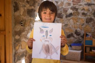 A boy in yellow holds up his drawing of an alien with cat ears. Mexico, 2011.