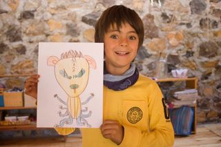 A boy holds up his drawing of a yellow alien with many legs. Mexico, 2011.