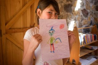 A girl holds up a pink sheet with a drawing of a green alien. Mexico, 2011.