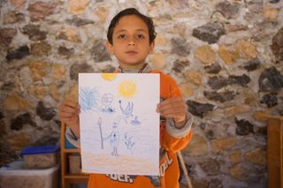 A boy holds up a blue drawing of figures under a yellow sun. Mexico, 2011.