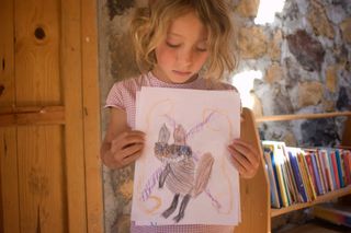 A girl looks down at her drawing of a brown alien with long arms. Mexico, 2011.