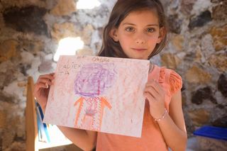 A girl holds up her drawing of a purple alien with orange legs. Mexico, 2011.