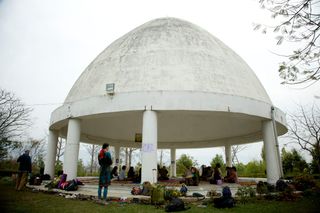 A white domed pavilion on a lawn, people sitting in its shade. Rishikesh, India, 2012.