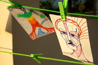 Two drawings of strange faces pegged on a green line. Rishikesh, India, 2012.