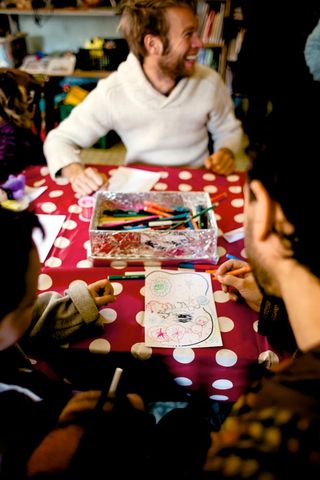 A smiling man at a table with a red spotted cloth and a box of pens. Spain, 2012.