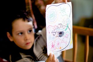 A boy holds up a drawing full of circles and patterns. Spain, 2012.
