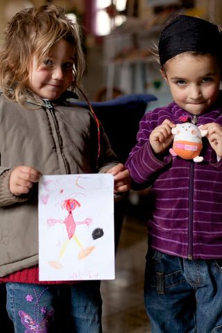 Two small children, one holding a drawing of a pink figure, the other a small toy. Spain, 2012.