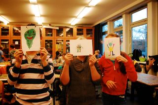 Three children hold large drawings in front of their faces, each showing a different colourful alien design. Germany, 2011.