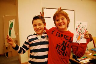 Two girls with red antenna headbands hold colourful alien drawings and smile at the camera. Germany, 2011.