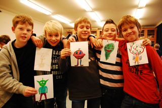 Five children with arms linked hold up various alien drawings, standing together in a school art room. Germany, 2011.
