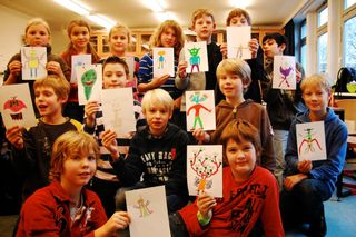 A boy in brown holds an alien drawing with three teal heads and red body sections. Germany, 2011.