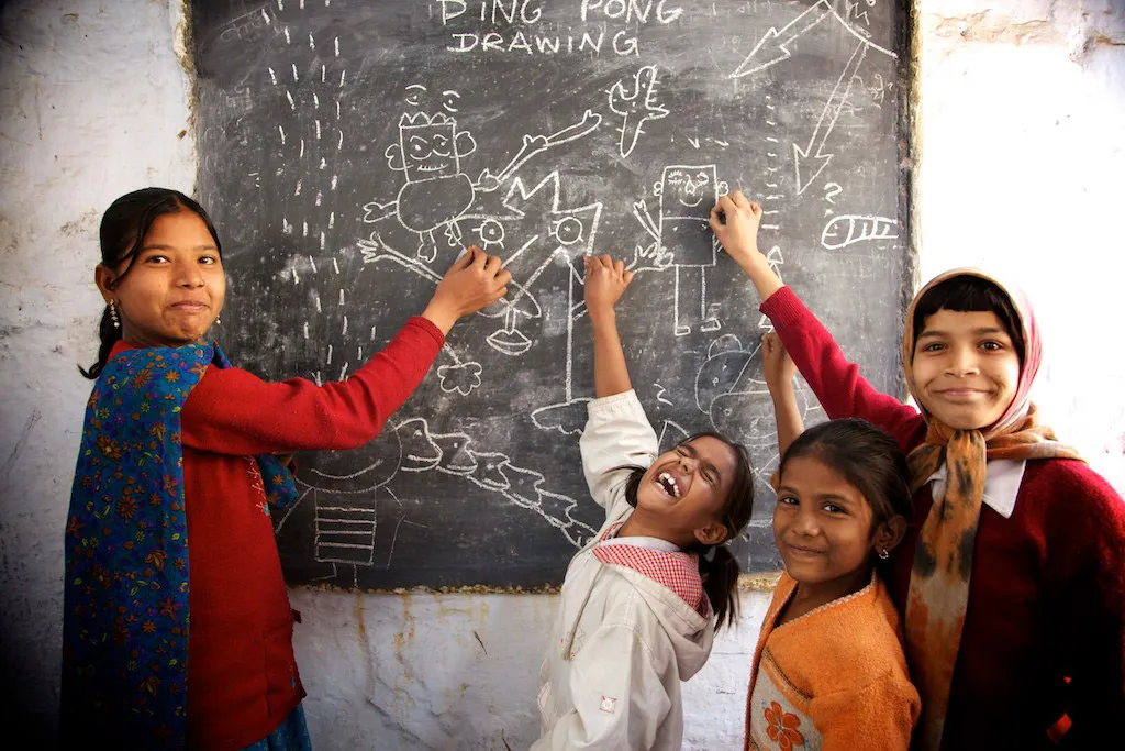 Children drawing together on a chalkboard headed Ping Pong Drawing.